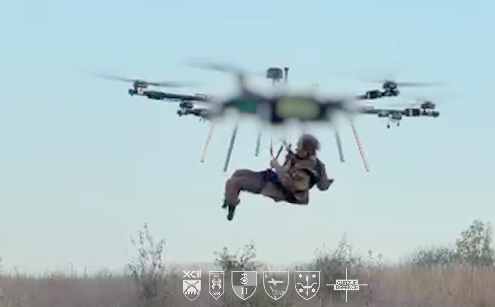 A heavy multirotor drone carries a wounded soldier suspended beneath it over open ground, in a frame from the 92nd Assault Brigade’s video